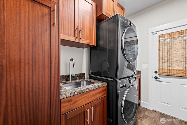 washroom featuring stacked washer and clothes dryer, cabinet space, a sink, and dark wood-style flooring