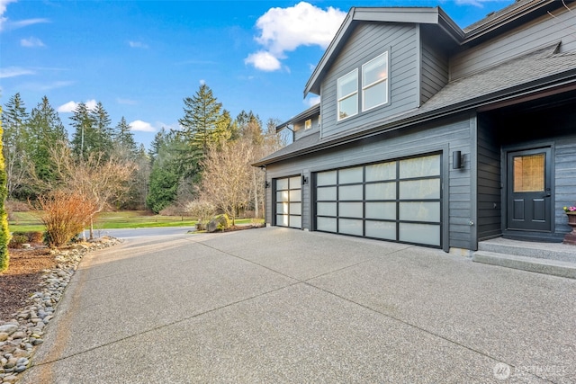 view of side of property featuring a garage, concrete driveway, and roof with shingles