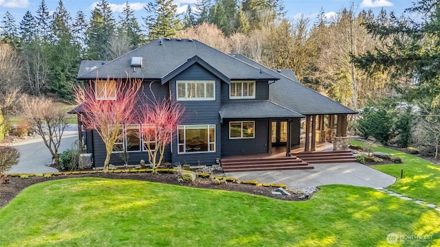 back of house featuring covered porch, a shingled roof, and a lawn