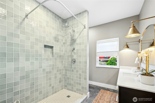 full bath featuring a tile shower, vanity, and baseboards