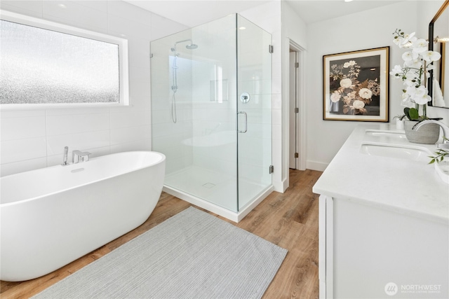 full bath with wood finished floors, tile walls, a soaking tub, a shower stall, and double vanity