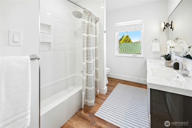 bathroom featuring double vanity, toilet, a sink, wood finished floors, and baseboards