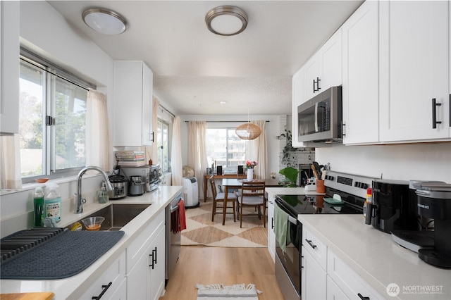 kitchen with stainless steel appliances, a sink, white cabinets, light countertops, and light wood finished floors