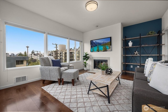 living area with a premium fireplace, wood finished floors, visible vents, and baseboards