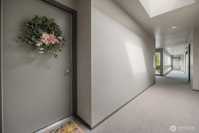 hall featuring light carpet, a skylight, and baseboards