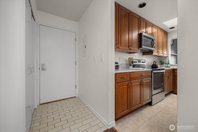 kitchen featuring stainless steel appliances, a skylight, baseboards, light countertops, and brown cabinets