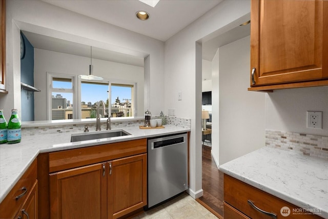 kitchen featuring light stone counters, hanging light fixtures, brown cabinetry, a sink, and dishwasher