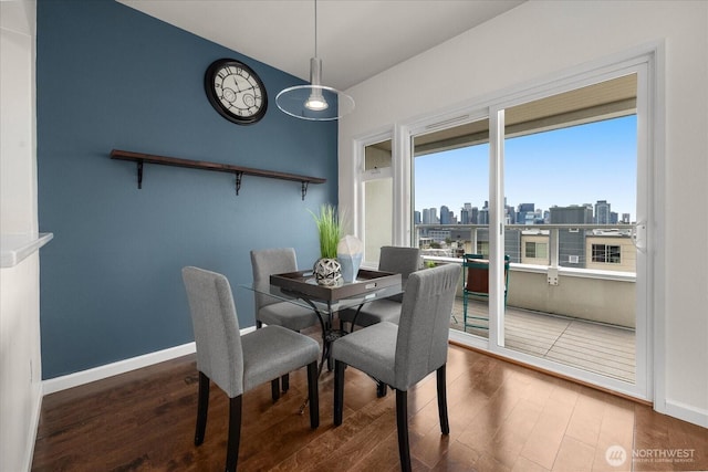 dining space with baseboards, vaulted ceiling, a city view, and wood finished floors