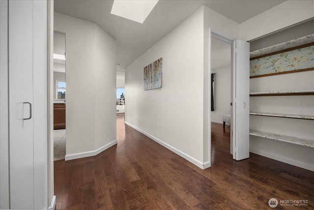 hallway with a skylight, baseboards, and dark wood-style flooring