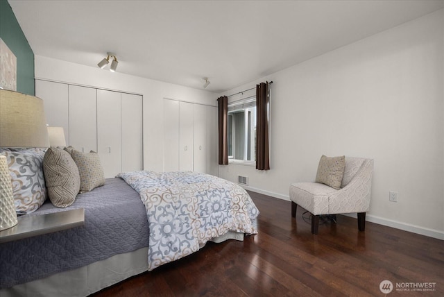 bedroom with baseboards, visible vents, hardwood / wood-style floors, and two closets