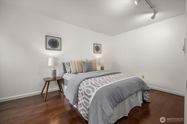 bedroom featuring dark wood-style flooring, rail lighting, and baseboards