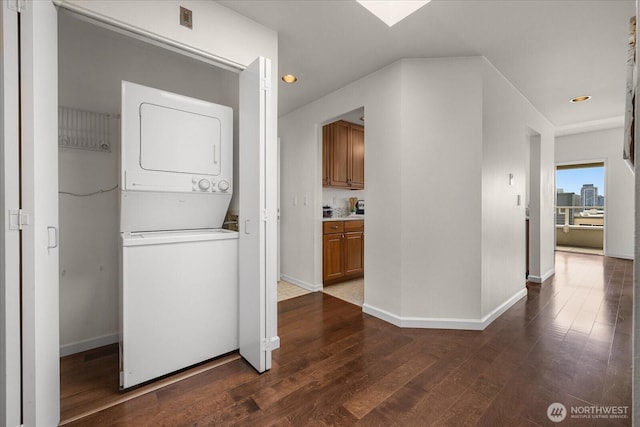 laundry room featuring stacked washer and dryer, recessed lighting, dark wood-type flooring, laundry area, and baseboards