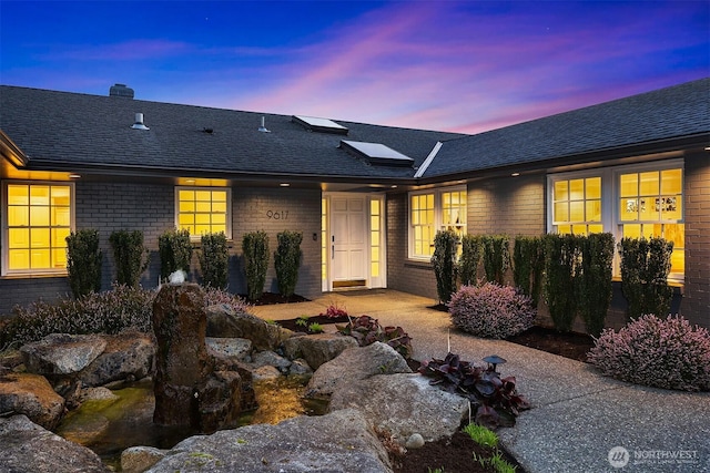 exterior space with a shingled roof, a chimney, solar panels, and brick siding