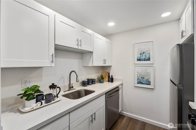 kitchen with stainless steel appliances, a sink, white cabinetry, light countertops, and dark wood-style floors