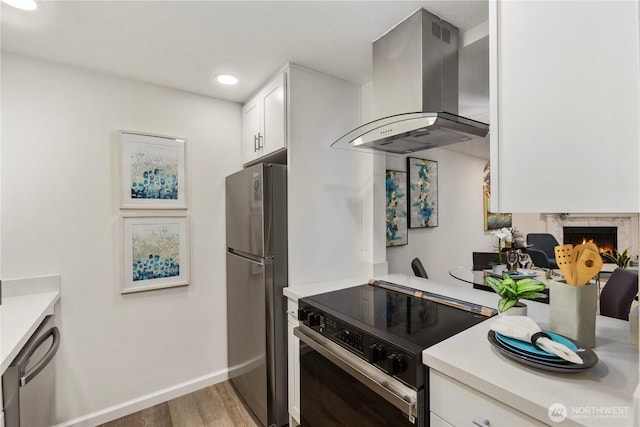 kitchen with island exhaust hood, stainless steel appliances, light countertops, a premium fireplace, and white cabinets