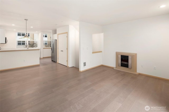 unfurnished living room with light wood-style floors, baseboards, a fireplace with raised hearth, and recessed lighting