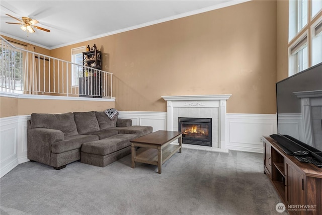 living room with carpet, wainscoting, crown molding, and a tile fireplace