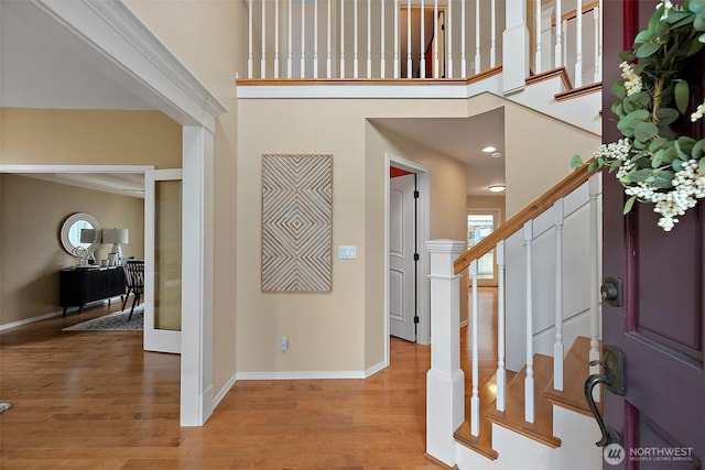 entryway featuring stairway, a towering ceiling, light wood-style flooring, and baseboards