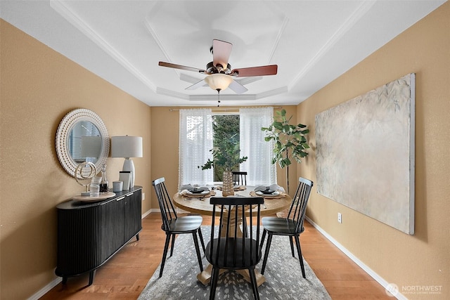 dining area with ceiling fan, light wood finished floors, a raised ceiling, and baseboards