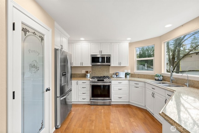 kitchen featuring appliances with stainless steel finishes, light countertops, light wood-style floors, white cabinetry, and a sink