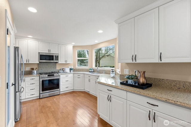 kitchen featuring stainless steel appliances, light wood finished floors, a sink, and white cabinets