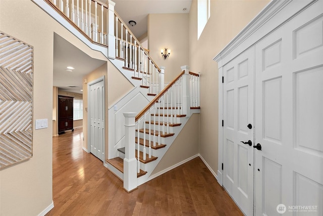 entrance foyer featuring hardwood / wood-style floors, stairway, a towering ceiling, and baseboards