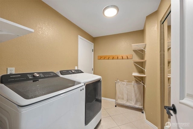 clothes washing area with laundry area, light tile patterned floors, a textured wall, and washing machine and clothes dryer