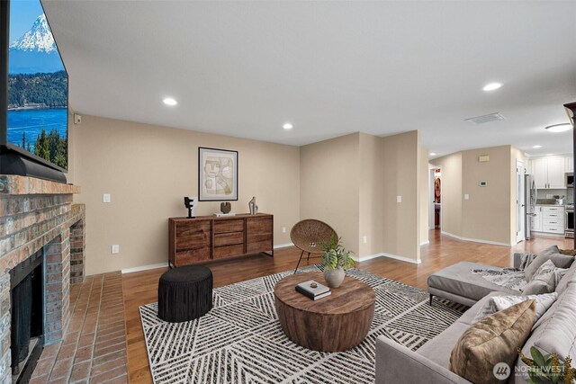 living area featuring recessed lighting, a brick fireplace, baseboards, and light wood finished floors