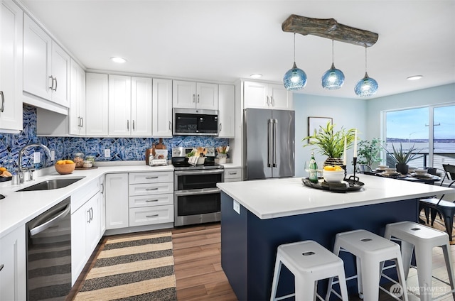 kitchen featuring wood finished floors, a sink, a kitchen breakfast bar, appliances with stainless steel finishes, and backsplash