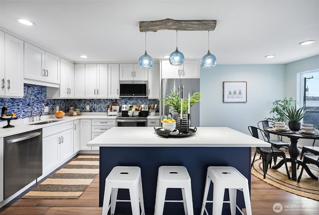 kitchen featuring wood finished floors, appliances with stainless steel finishes, a sink, and a kitchen breakfast bar