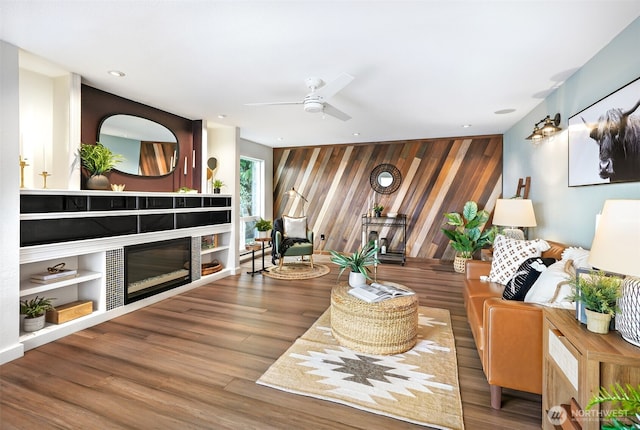 living area with recessed lighting, a tiled fireplace, an accent wall, a ceiling fan, and wood finished floors