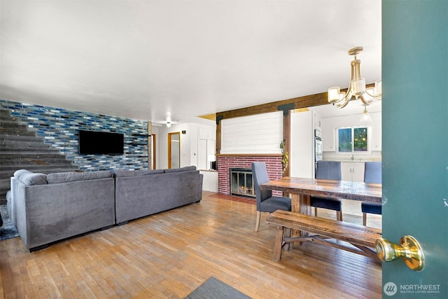 living area with a brick fireplace, light wood-style floors, an accent wall, and a chandelier