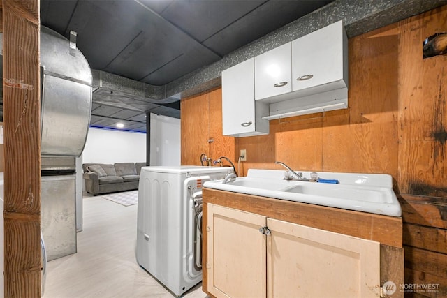 laundry area featuring washer / clothes dryer, cabinet space, light wood-style flooring, wood walls, and a sink