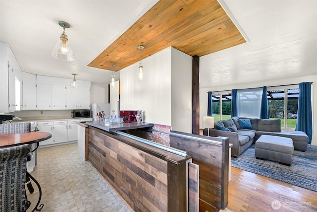 kitchen featuring decorative light fixtures, stainless steel microwave, freestanding refrigerator, open floor plan, and white cabinetry