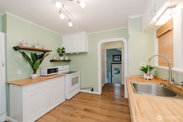 kitchen with arched walkways, white appliances, butcher block countertops, a sink, and white cabinetry