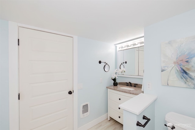 half bathroom featuring heating unit, toilet, vanity, wood finished floors, and baseboards