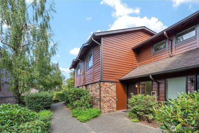 view of property exterior with brick siding and a shingled roof