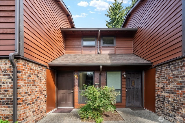 view of exterior entry with brick siding and a shingled roof