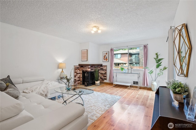 living room featuring a textured ceiling, a fireplace, visible vents, and wood finished floors