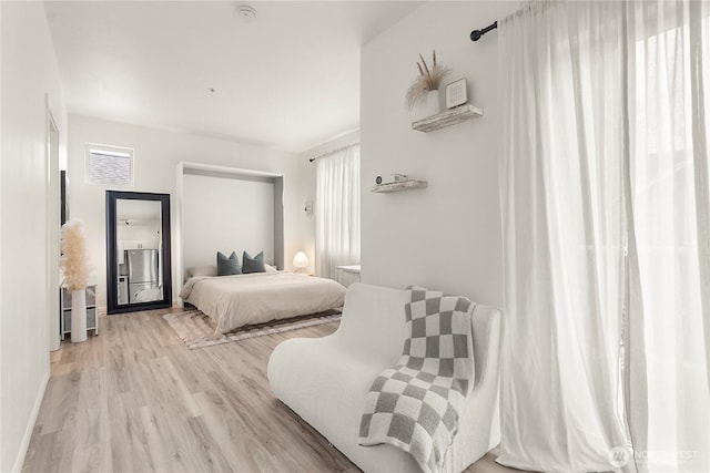 bedroom featuring light wood-style floors, freestanding refrigerator, and baseboards