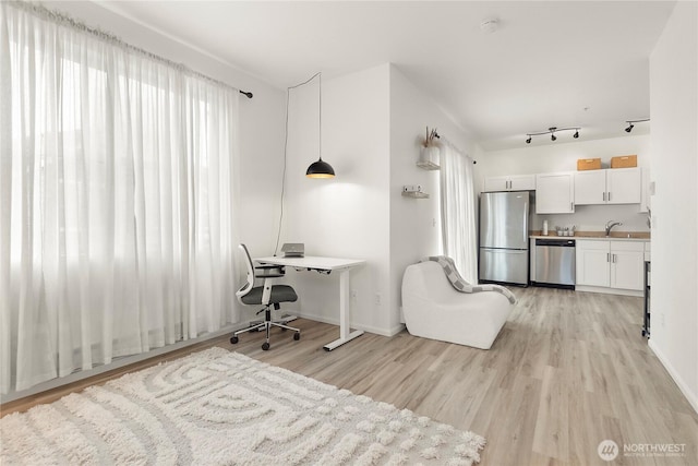 office area featuring rail lighting, a sink, light wood-style flooring, and baseboards