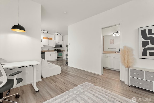 office space featuring light wood finished floors, baseboards, a sink, and rail lighting