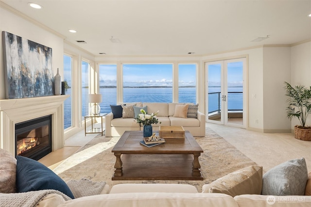 carpeted living area featuring crown molding, recessed lighting, a water view, a glass covered fireplace, and baseboards