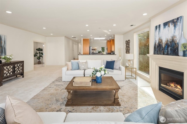 living area featuring recessed lighting, a glass covered fireplace, crown molding, and baseboards