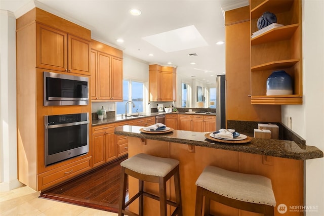 kitchen featuring recessed lighting, a sink, a peninsula, a kitchen bar, and appliances with stainless steel finishes