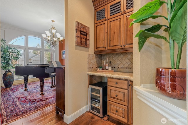 bar with beverage cooler, baseboards, decorative backsplash, wood finished floors, and hanging light fixtures