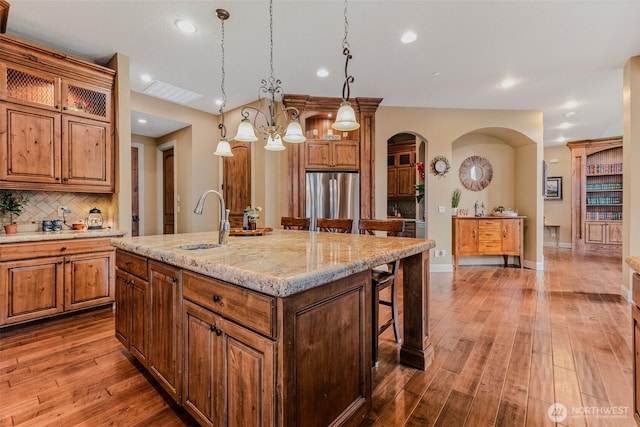 kitchen with arched walkways, brown cabinets, freestanding refrigerator, decorative backsplash, and a kitchen bar