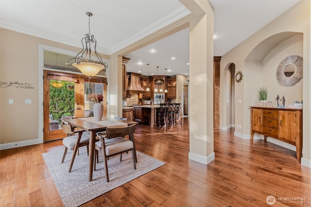 dining area featuring arched walkways, recessed lighting, baseboards, hardwood / wood-style floors, and crown molding