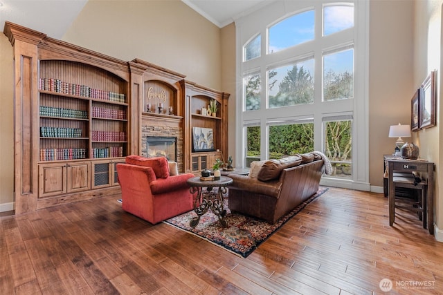 living area featuring a high ceiling, a fireplace, wood finished floors, and baseboards