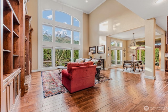 living room with light wood-type flooring, a high ceiling, and crown molding